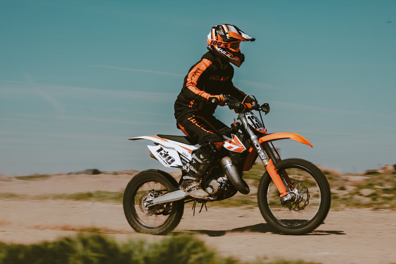 gallery-3 A rider on a dirtbike speeds through a rugged motocross terrain under a clear sky.